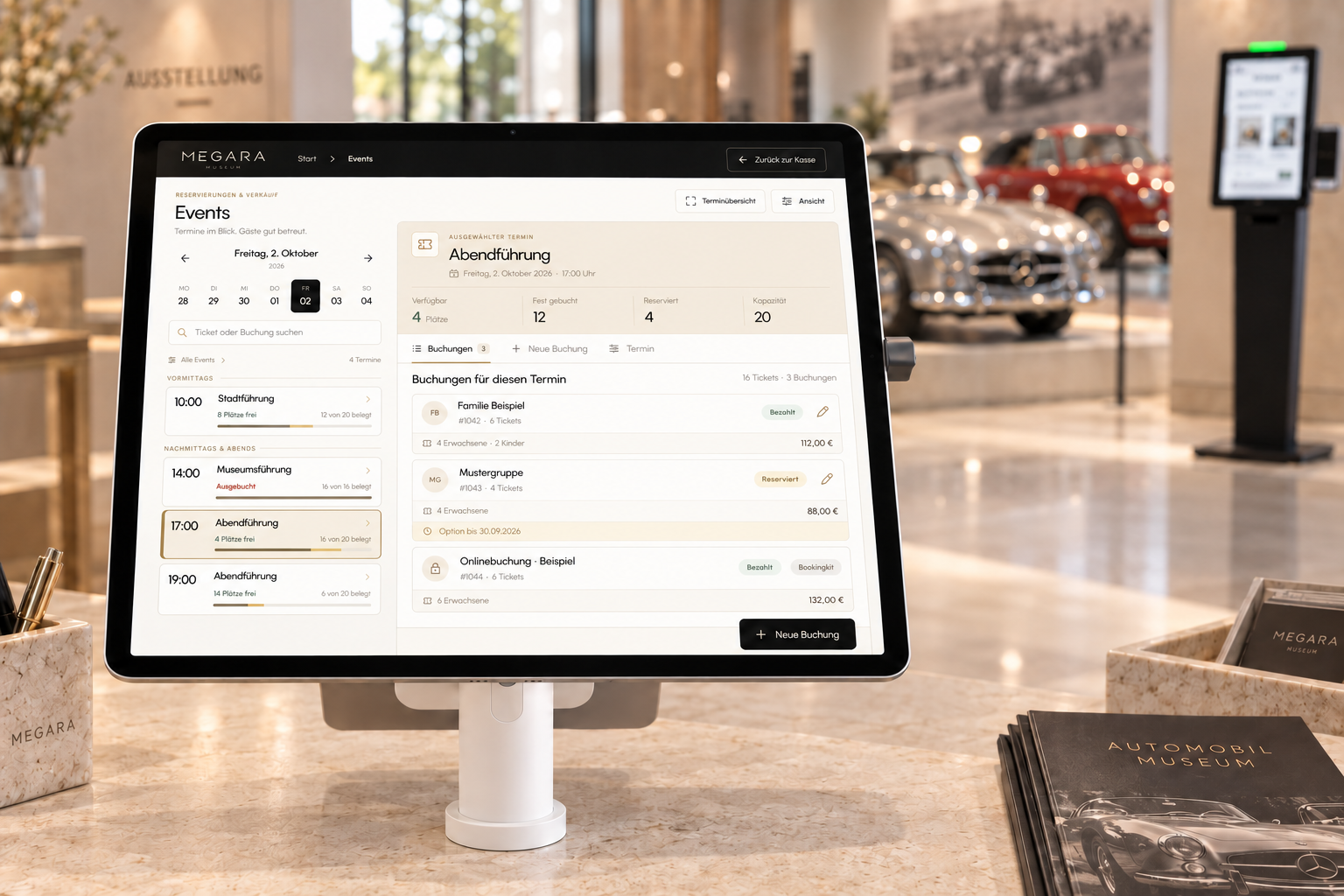 Megara-Buchungsübersicht auf einem iPad in weißer Bouncepad-Halterung am Ticketcounter eines Automobilmuseums, aus Sicht des Personals. Im Hintergrund stehen Oldtimer und ein SelfOrder-Terminal.